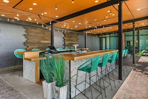 A modern bar area with a wooden bar counter, green chairs, and a brick wall. - The Landing at Hampton Marina, Tapestry Collection by Hilton (Hampton)