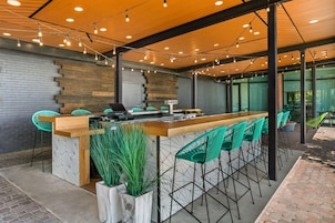 Un área de bar moderna con mostrador de madera, sillas verdes y pared de ladrillo.