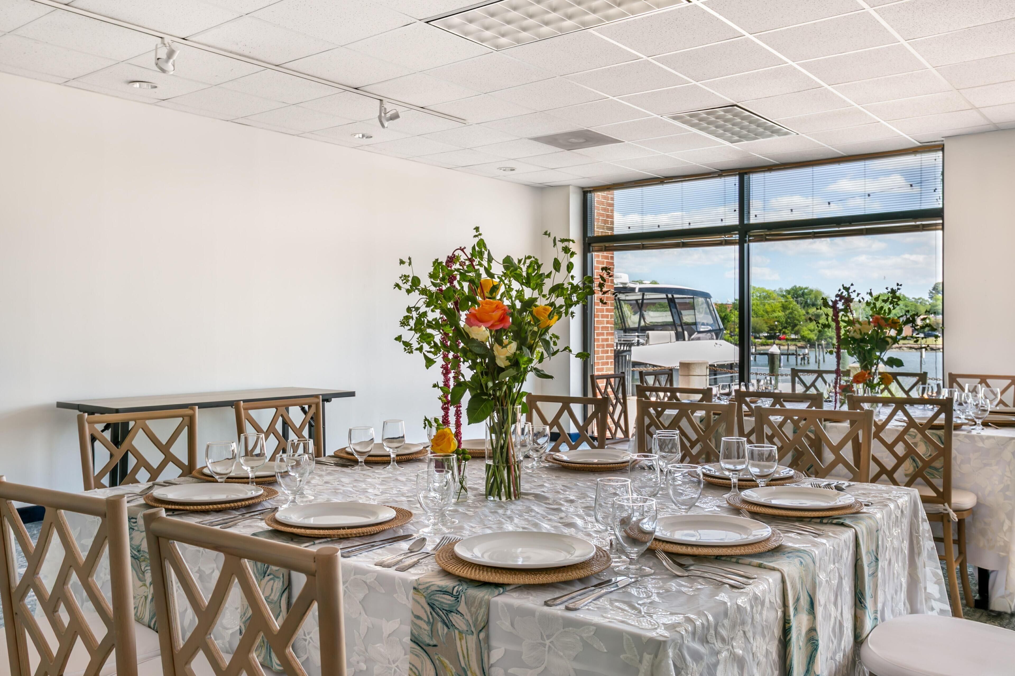 A dining area with tables set for a meal, featuring a view of the outdoors through large windows.