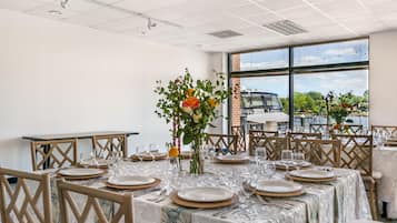 A dining area with tables set for a meal, featuring a view of the outdoors through large windows.