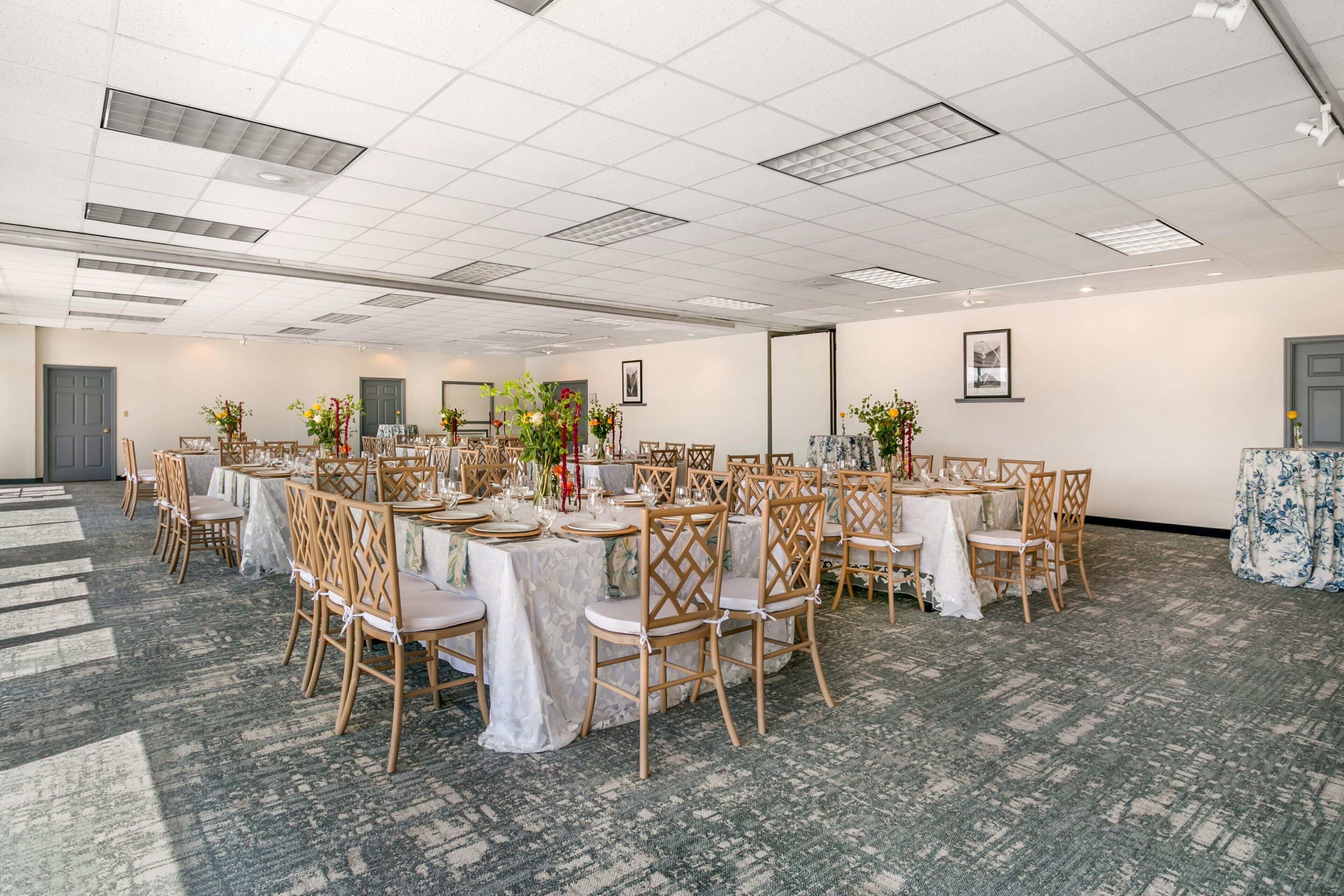 A conference room with round tables, wooden chairs, and floral centerpieces.
