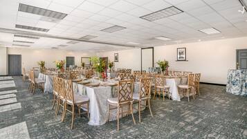 Sala de conferências com mesas redondas, cadeiras de madeira e centros de mesa florais.