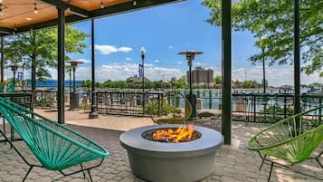 An outdoor seating area with a fire feature, chairs, and a view of a body of water and buildings.