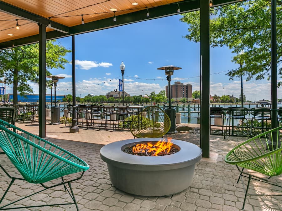 Un espacio de estar al aire libre con una chimenea, sillas y vistas a un cuerpo de agua y edificios.