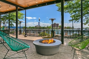 Un espacio de estar al aire libre con una chimenea, sillas y vistas a un cuerpo de agua y edificios.