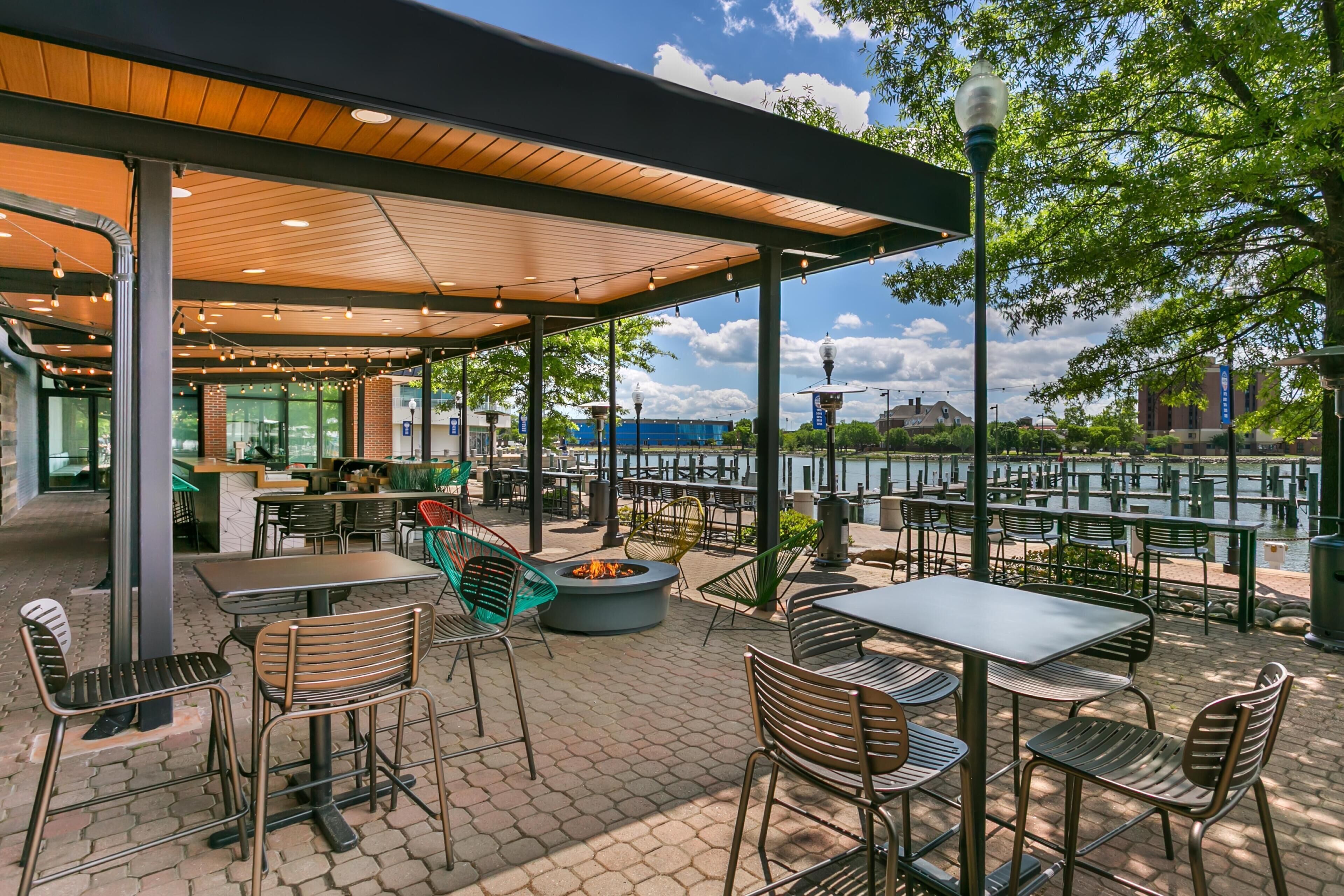 An outdoor patio with tables and chairs, a fire pit, and a view of a body of water.