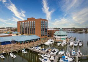 Un puerto deportivo con barcos amarrados, un edificio con techo azul y una gran construcción de ladrillo con ventanas verticales.