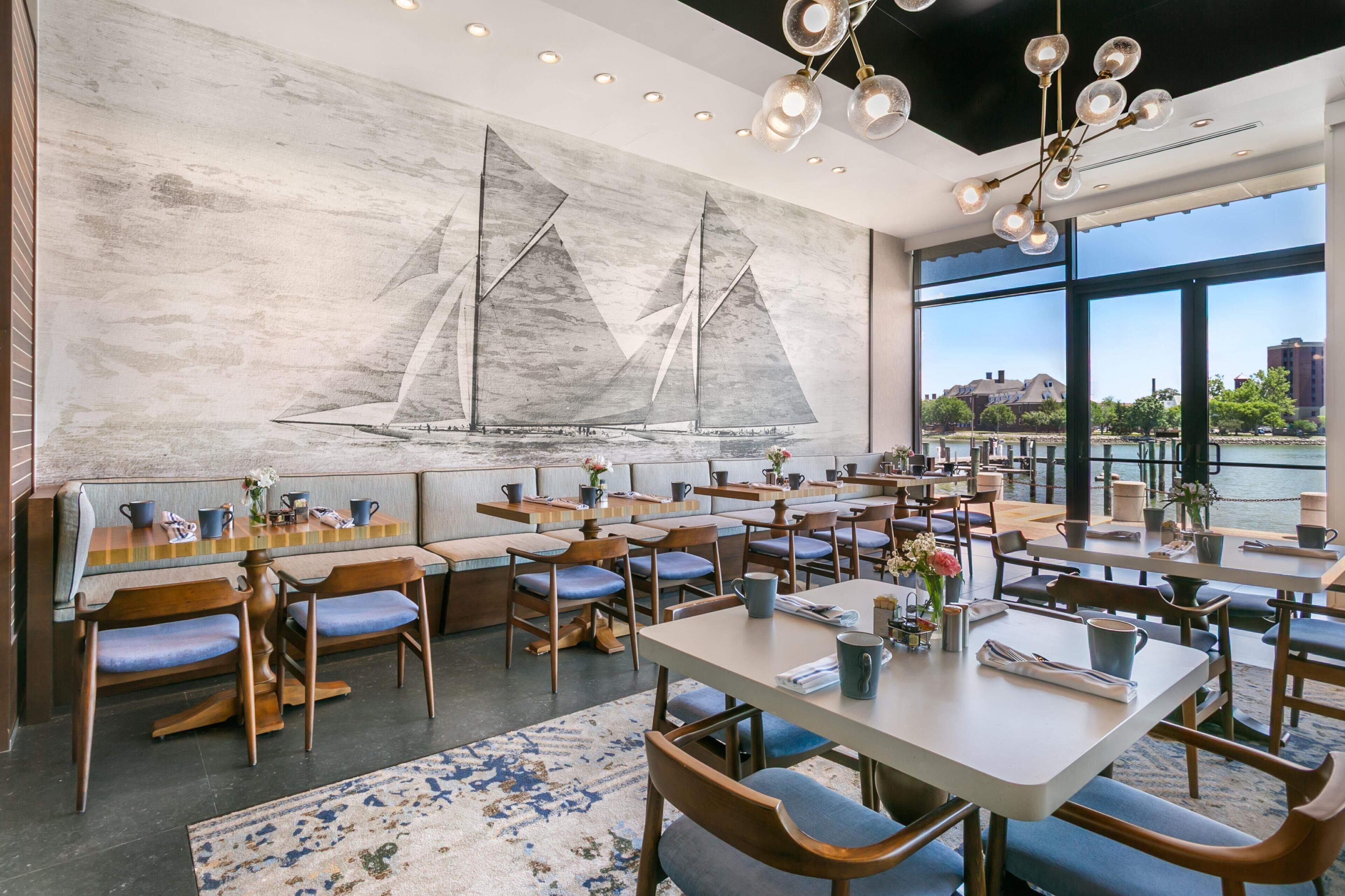 Un restaurant décoré d’une fresque murale sur le thème de la marine, doté de plusieurs espaces de restauration et de grandes fenêtres offrant une vue sur la ville.