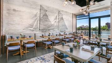 Ein Restaurant mit einer nautisch gestalteten Wandmalerei, verschiedenen Sitzbereichen und großen Fenstern, die einen Blick auf die Stadt ermöglichen.
