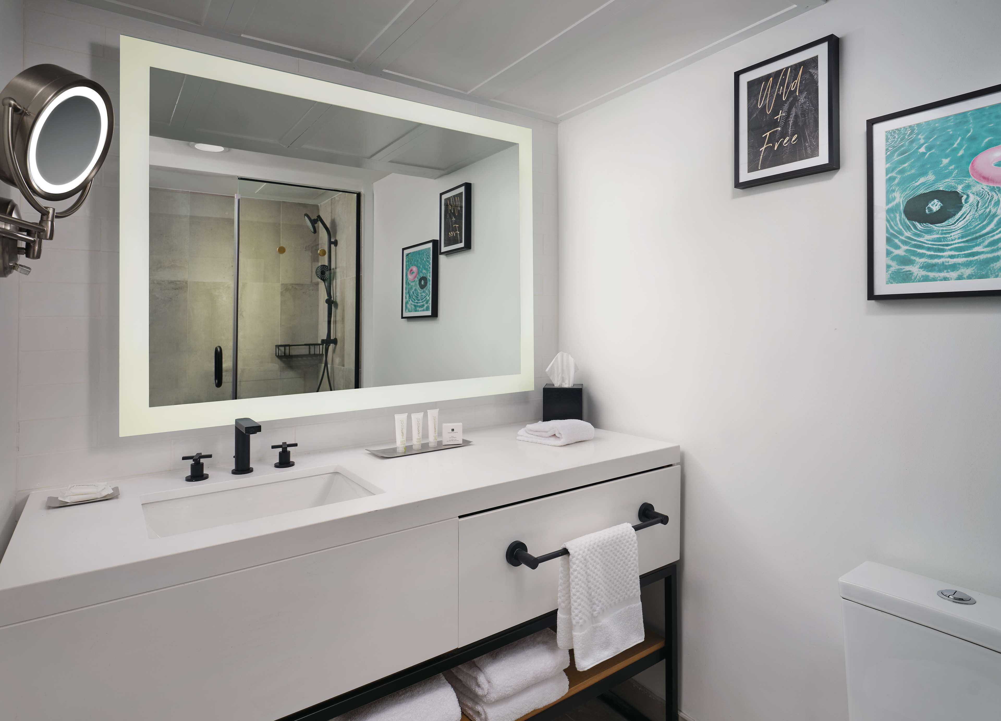 Une salle de bain moderne avec un grand miroir, une douche, des toilettes et un porte-serviettes.