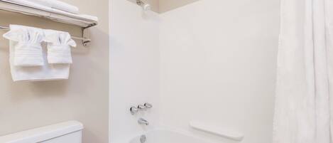 A bathroom with a bathtub, a toilet, and a towel rack with towels.