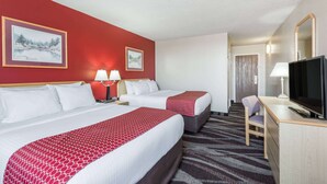 Ein Hotelzimmer mit zwei Betten, einem Schreibtisch, einem Fernseher und zwei Bildern an der Wand.