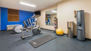 Ein Fitnessraum mit Trainingsgeräten, einem Yogaball, einem Wasserspender und einem Mülleimer.