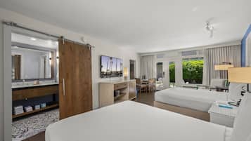Habitación de hotel con una cama grande, un escritorio con silla, televisión, baño con espejo y vistas a zonas verdes.