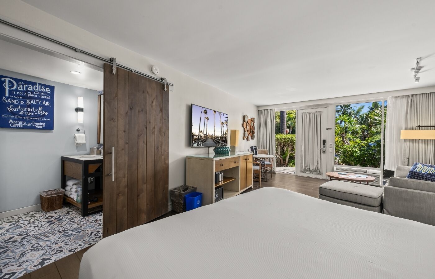 A modern hotel room with a large bed, a desk with a computer, a TV, and a view of the outdoors.