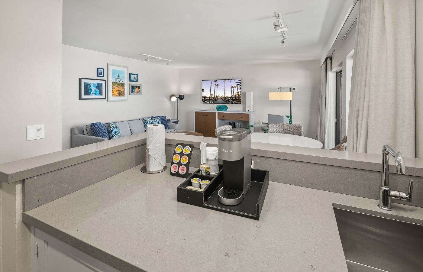 Una habitación de hotel moderna con kitchenette, una zona de estar con sofá y sillones, un ventanal con vistas y un minibar.