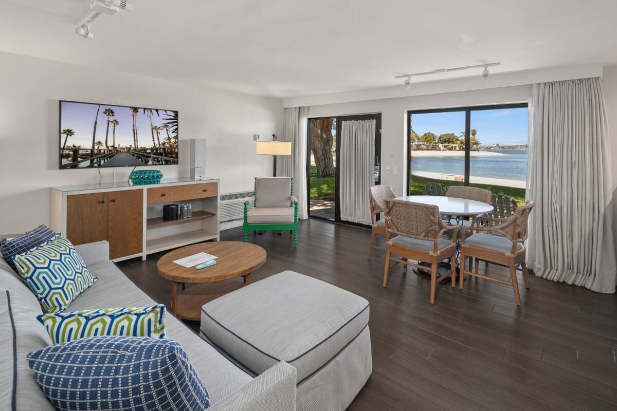 A modern hotel room with a living area, a dining table, and a view of the beach.