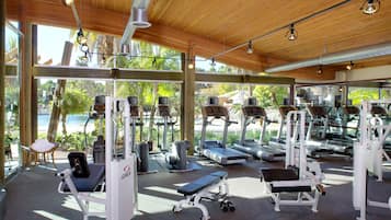A gym with various exercise equipment, large windows, and a wooden ceiling.