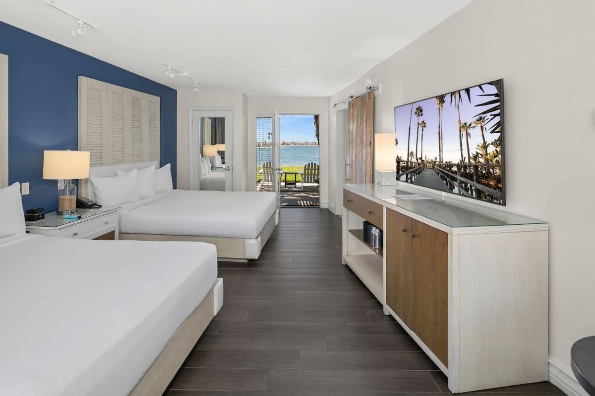A hotel room with two beds, a minibar, a TV, and a view of the sea.