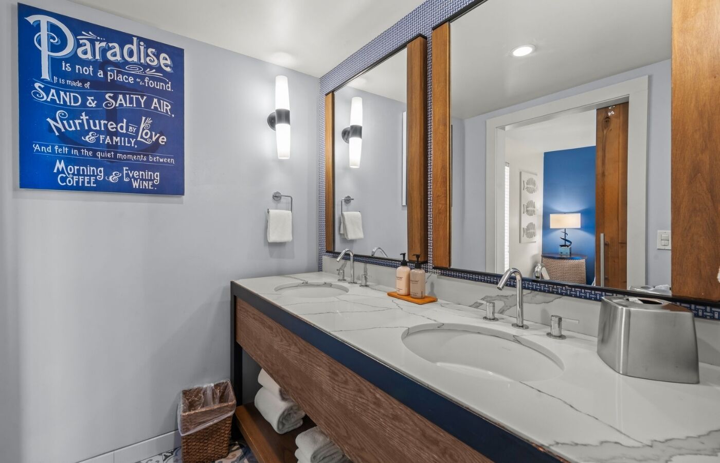 Un baño moderno con dos lavamanos, un espejo grande y un cartel en la pared.