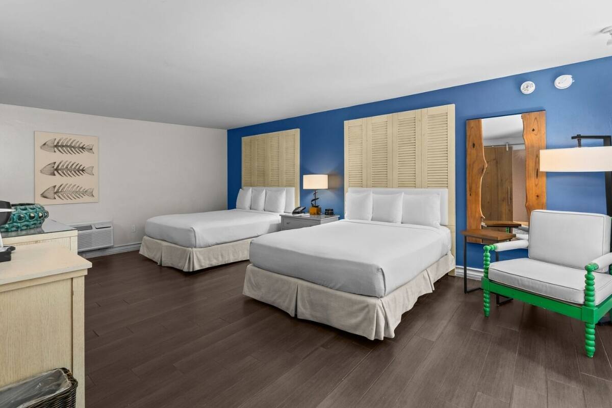 A hotel room with two single beds, a desk with a lamp, a chair, and a mirror.