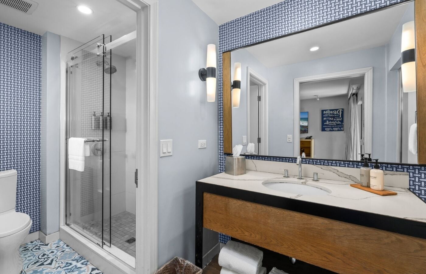 A modern bathroom with a glass-enclosed shower, a large mirror, and a wooden vanity with a marble countertop.