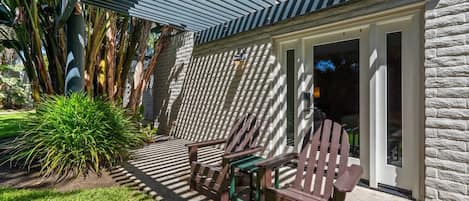 Eine Terrassenfläche mit Adirondack-Stühlen, einem kleinen Tisch und einer Steinmauer.