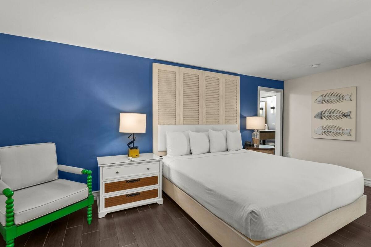 A bedroom with a bed, a nightstand, a chair, and a wall with artwork.