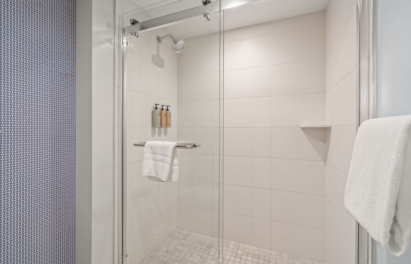 Um chuveiro moderno com porta de vidro, azulejos brancos e um porta-toalhas com toalha.