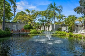 A tranquil pond with a fountain, surrounded by lush greenery and a building with a white facade. - Paradise Point Resort & Spa (San Diego)