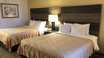 A hotel room with two beds, a nightstand with a lamp, a framed picture on the wall, and a carpeted floor.