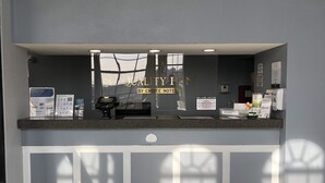A hotel reception desk with a glass partition, a digital payment terminal, informational brochures, and a sign welcoming visitors. - Quality Inn Bennettsville (Bennettsville)
