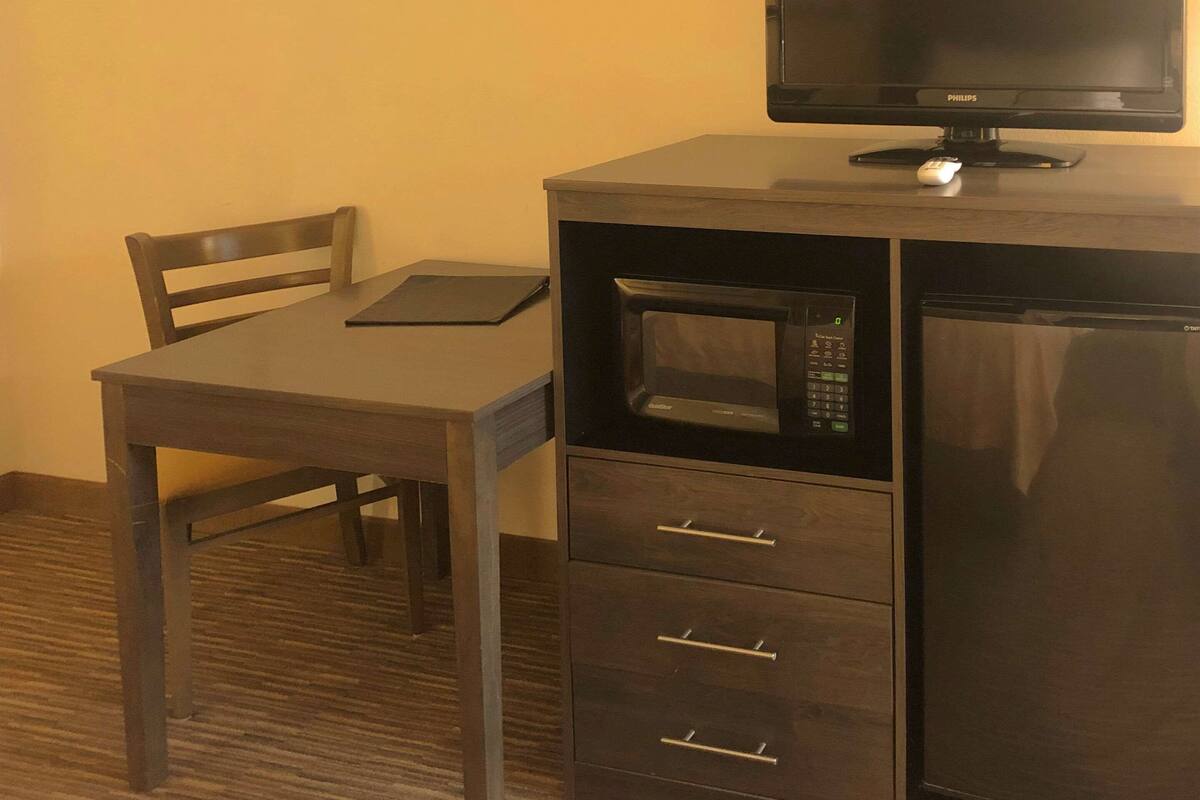 A compact, dark-colored desk with a flat-screen monitor, a built-in microwave, and a small refrigerator.
