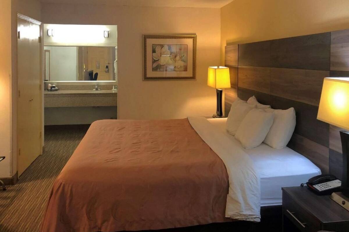 A hotel room with a bed, bedside lamps, a nightstand, a mirror, and a framed picture on the wall.