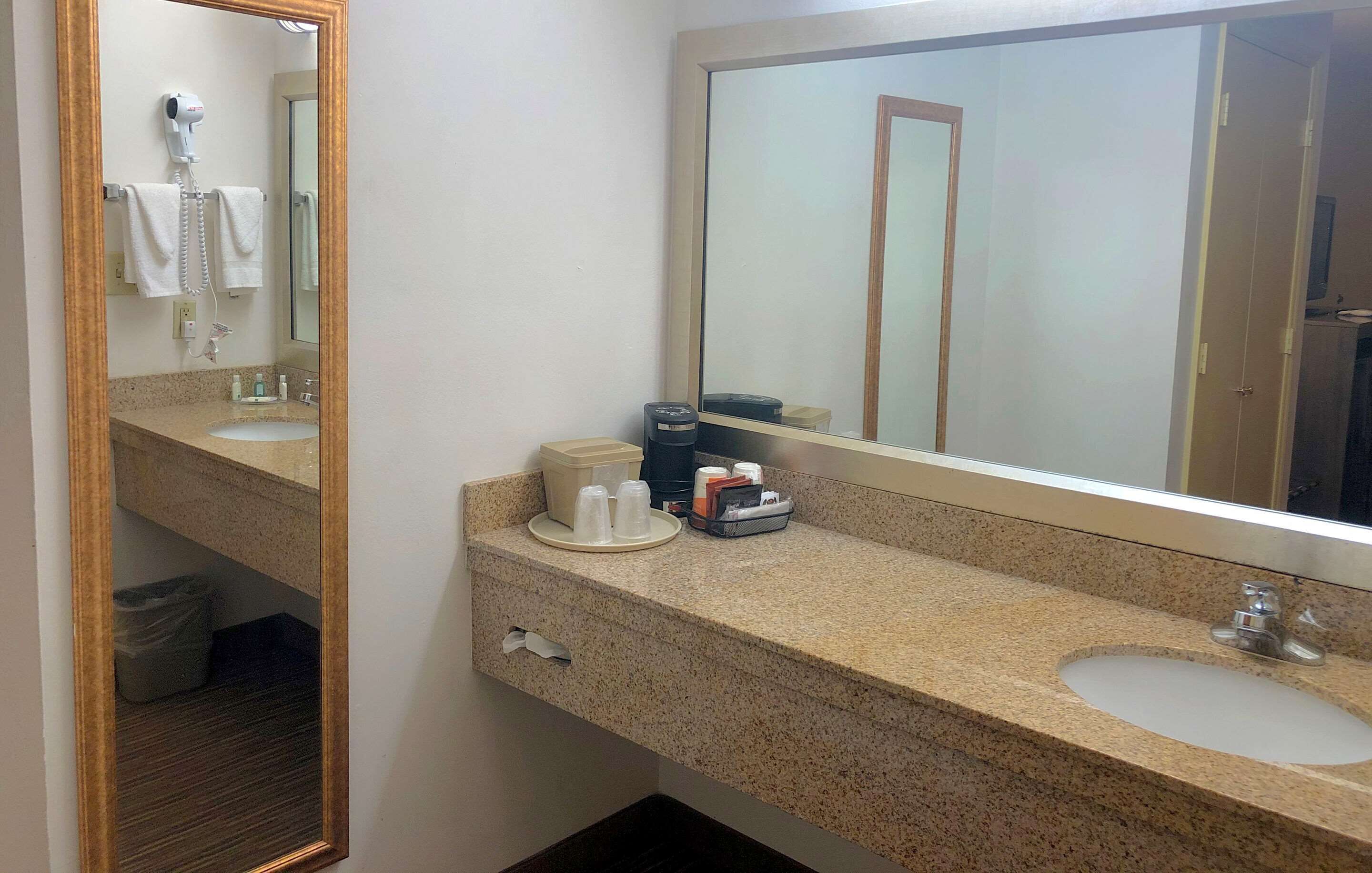 Een hotelbadkamer met een granieten aanrecht, een wastafel, een spiegel, een haardroger en toiletartikelen.