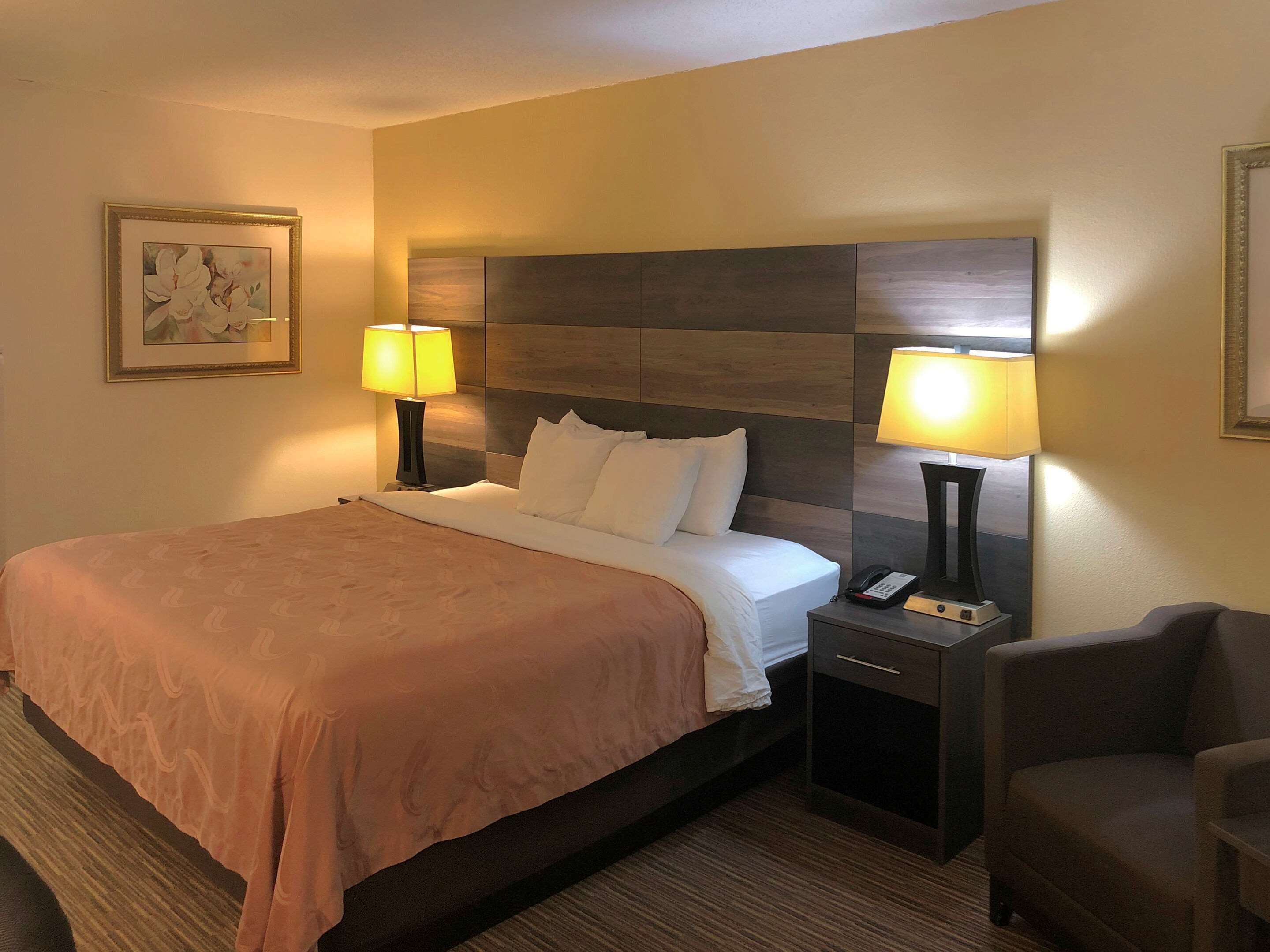 Habitación de hotel con una cama grande, dos lámparas de noche, una mesita de noche con teléfono y una silla.