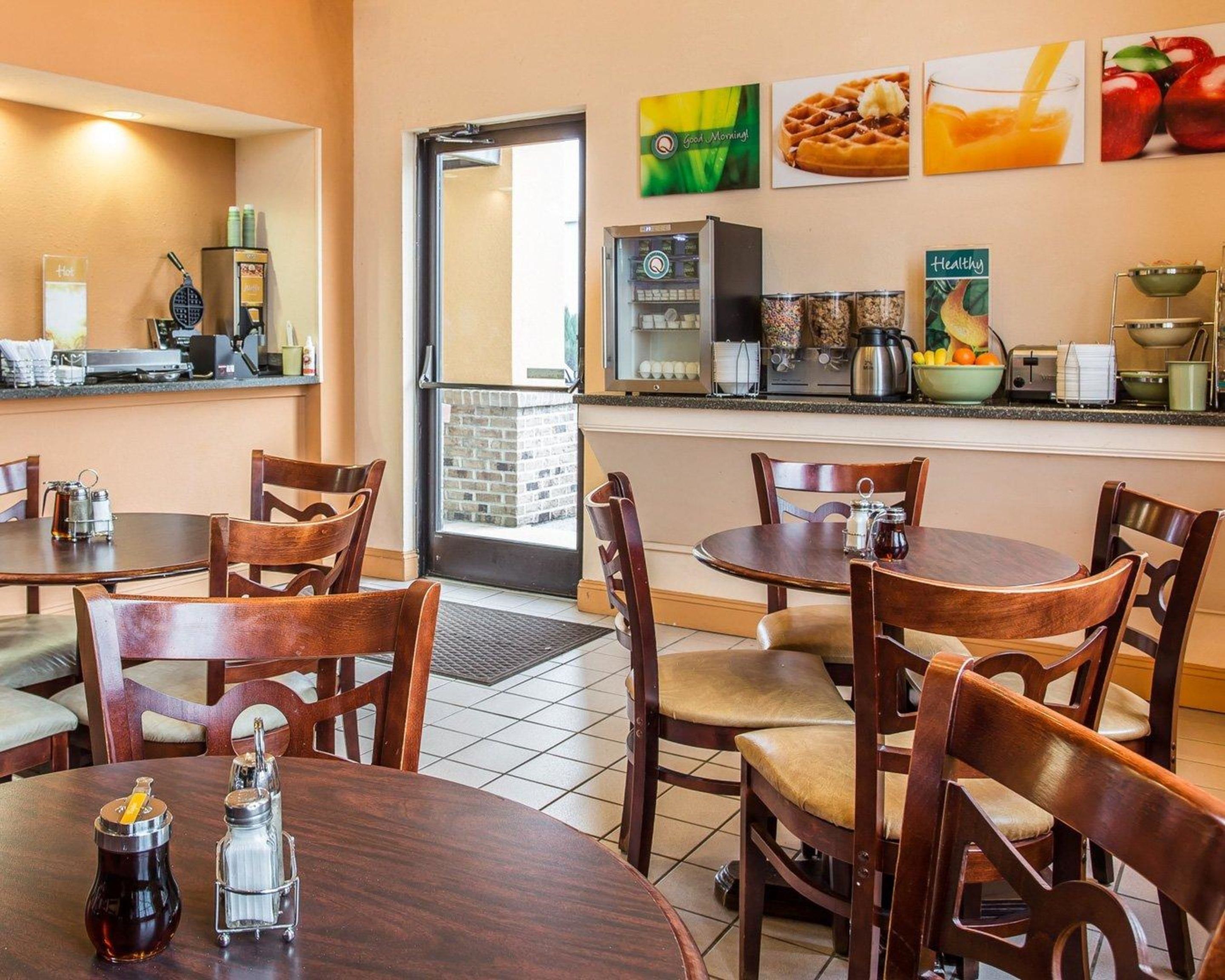 Um restaurante com mesas e cadeiras de madeira, uma máquina de café e um frigorífico.