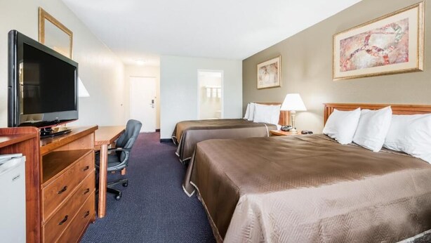 Une chambre d’hôtel avec deux lits, un bureau équipé d’une télévision, une chaise et une lampe.