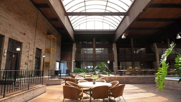 A spacious indoor area with a high ceiling and skylight, featuring multiple tables and chairs, brick walls, and potted plants. - Quality Inn Somerset (Somerset)