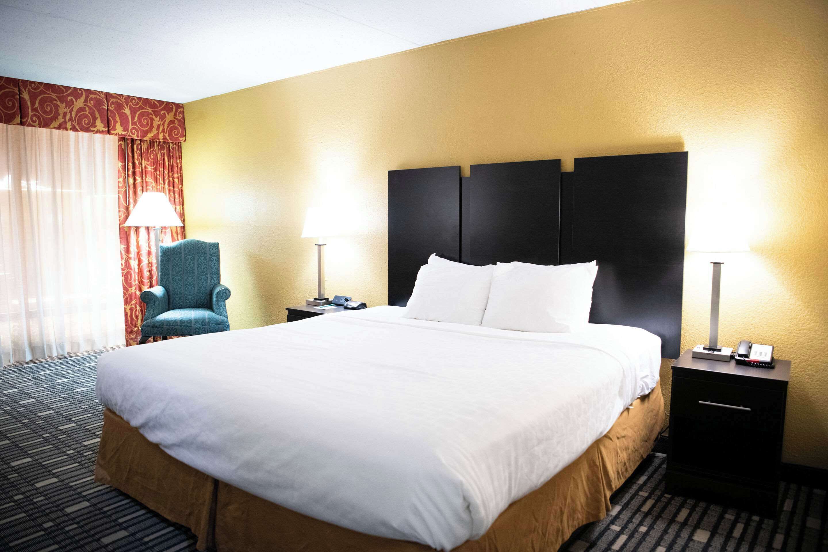 A hotel room with a large bed, two bedside tables, a chair, and a lamp.