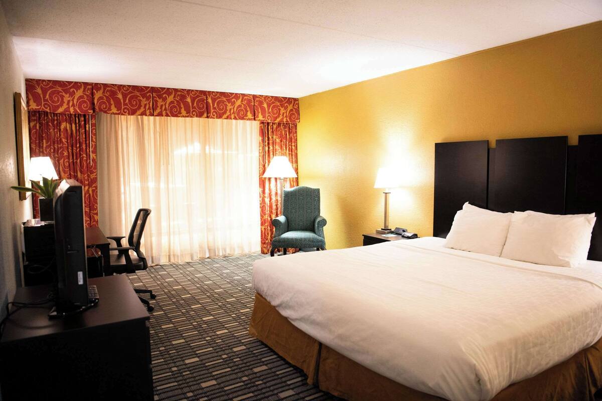 Quarto de hotel com uma cama grande, uma escrivaninha com computador, uma cadeira e duas luminárias.