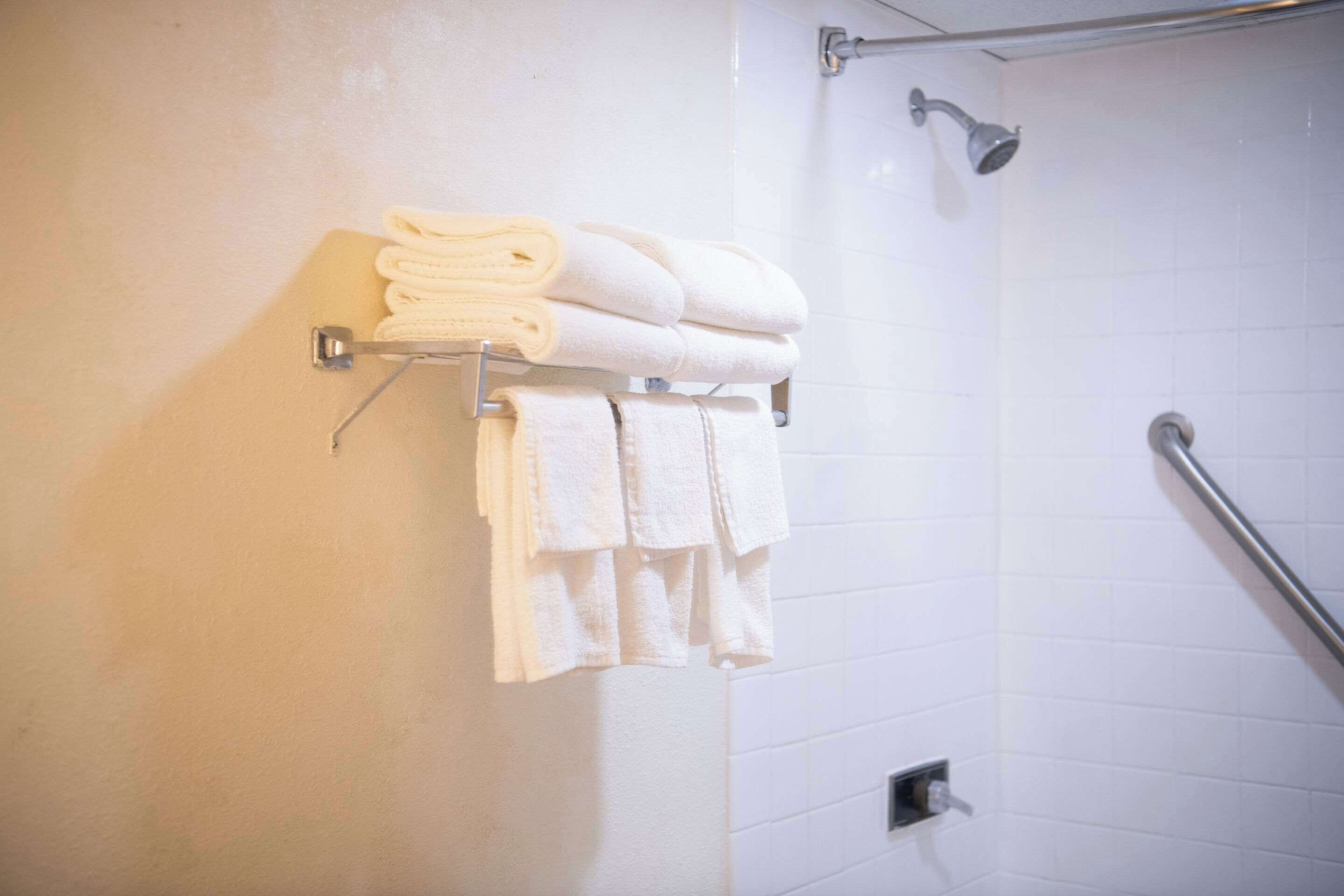 A bathroom with white tiled walls, a shower with a handheld showerhead, and a towel rack with neatly folded towels.