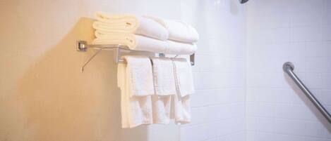 A bathroom with white tiled walls, a shower with a handheld showerhead, and a towel rack with neatly folded towels.