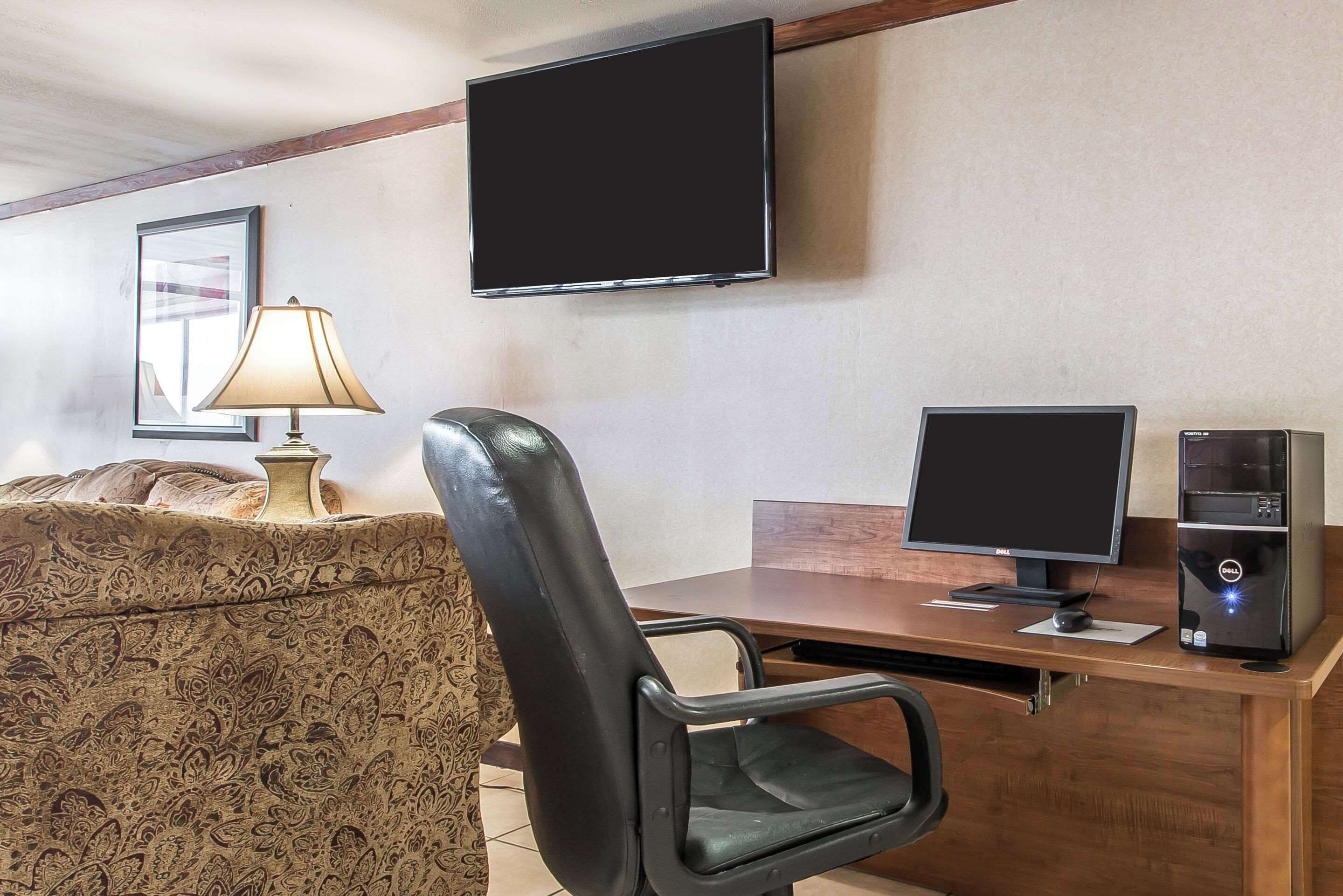 A hotel room with a bed, a desk with a computer, a TV, and a lamp.