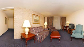 A hotel room with a sofa, two armchairs, a coffee table, a TV, and a lamp.