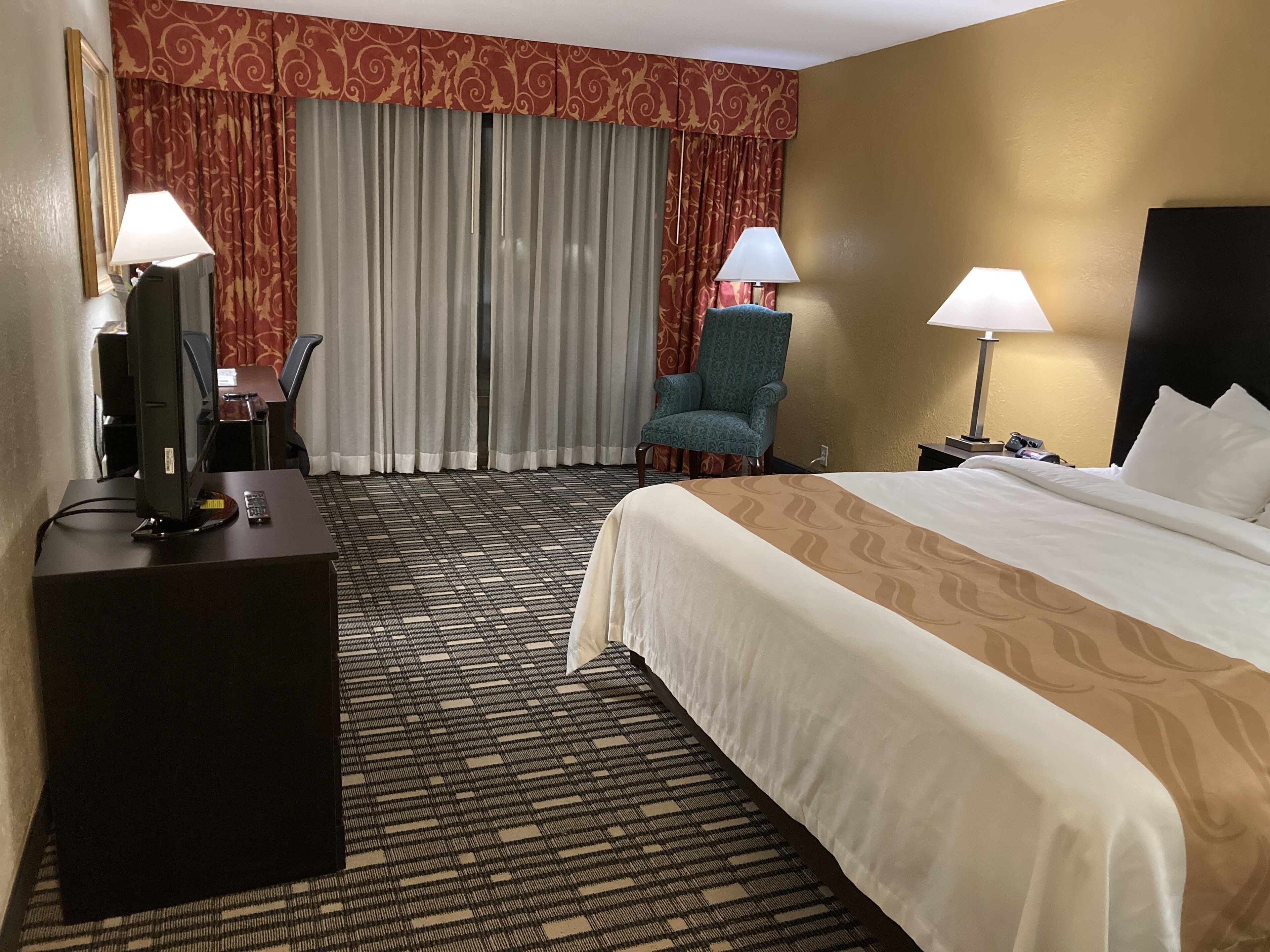 A hotel room with a bed, a desk with a computer, a chair, and two lamps.