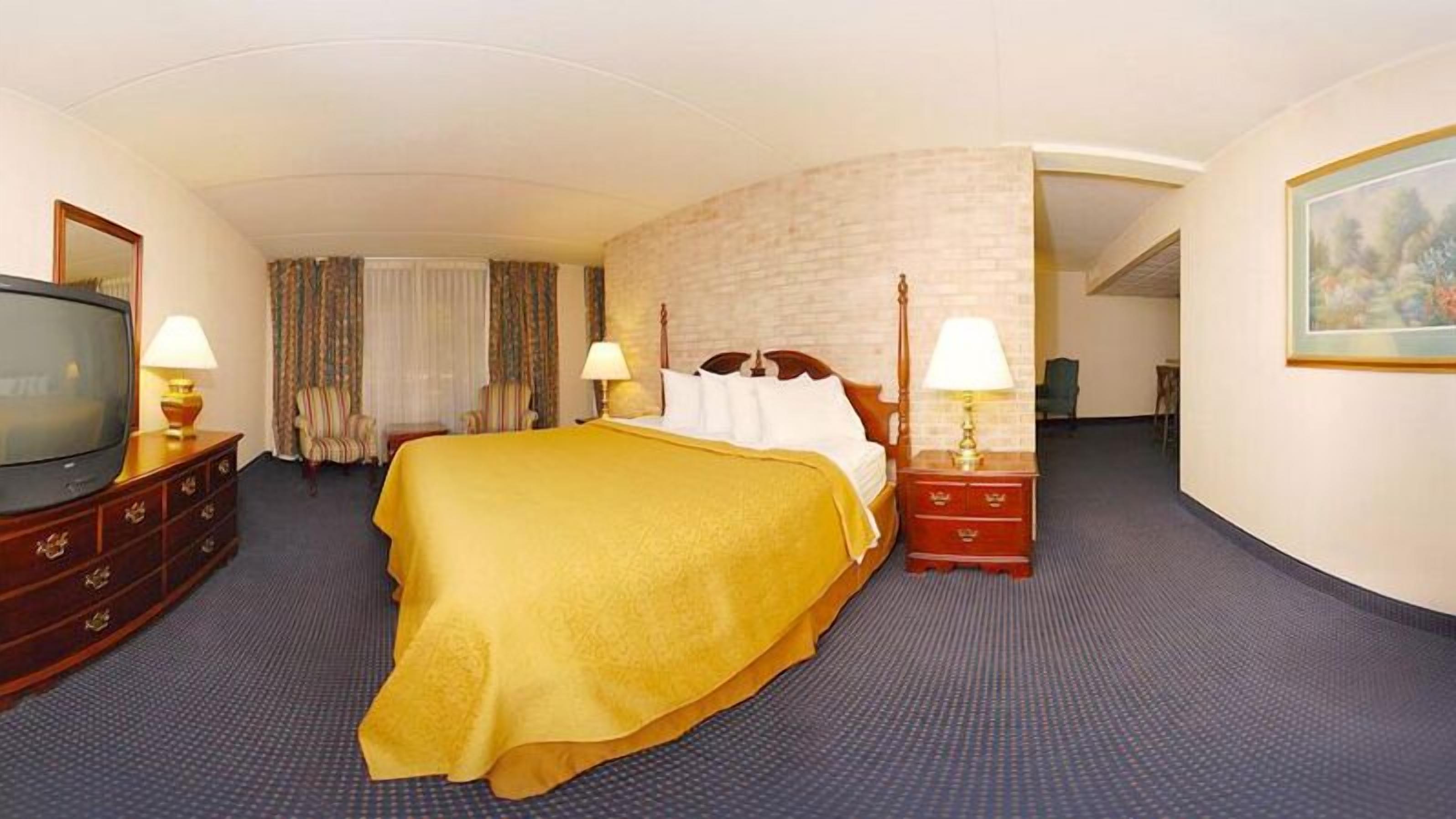 Habitación de hotel con una cama grande, dos mesitas de noche con lámparas, un televisor en una cómoda y un cuadro en la pared.