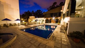 A swimming pool with lounge chairs and umbrellas, surrounded by a paved patio area.