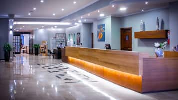 Un moderno vestíbulo de hotel con un mostrador de recepción, una cafetera y un área de descanso con sillas y una mesa.