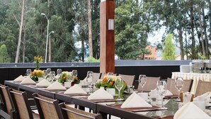 A dining area with tables set for a meal, surrounded by chairs, with a view of trees and buildings in the background. - Oro Verde Cuenca (Cuenca)